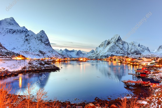 Wzornik fototapety o porze zimowej przedstawiająca ośnieżone góry, jezioro i czerwone krzewy zdobiące norweski krajobraz. Fototapeta do pokoju dziennego, sypialni, salonu, biura, gabinetu, przedpokoju i jadalni.