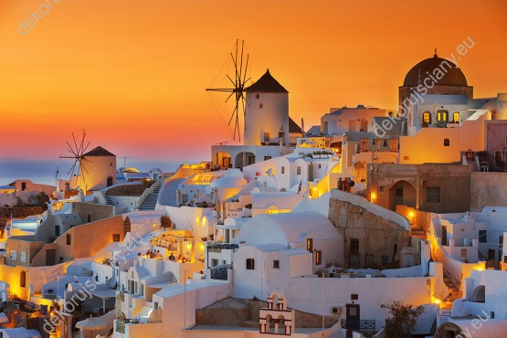 Wzornik fototapety z widokiem na miasto w Grecji o zachodzie słońca. Budynki mają charakterystyczną zabudową śródziemnomorską. Fototapeta do salonu, sypialni, pokoju dziennego, gabinetu, biura, przedpokoju.
