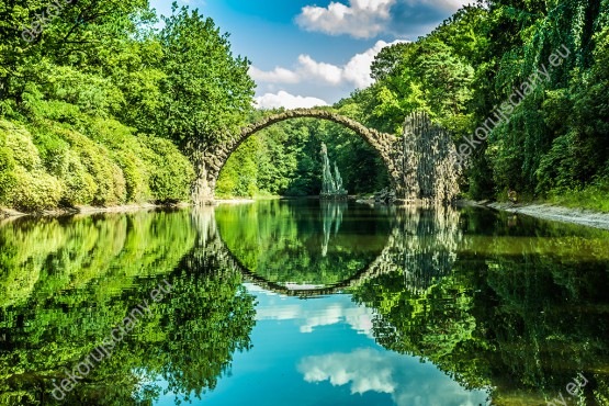 Wzornik fototapety przedstawia kamienny most w nad wodą, w wiosennych barwach soczystej zieleni. Miejsce - Kromlau w Niemczech. Fototapeta przeznaczona do sypialni, salonu, biura, gabinetu, pokoju młodzieżowego.