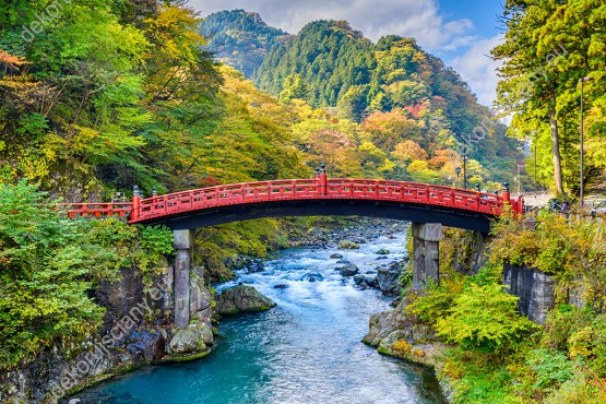 Wzornik fototapety z widokiem na czerwony most nad rzeką, wśród jesiennych, górskich lasów w Japonii. Fototapeta do pokoju dziennego, sypialni, salonu, biura, gabinetu, przedpokoju i jadalni.
