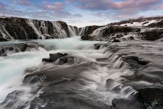 Wzornik fototapety z widokiem na szalejące wodospady Islandii spływające po kamieniach. Fototapeta do pokoju dziennego, sypialni, salonu, biura, gabinetu, przedpokoju i jadalni.
