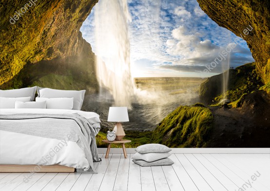 Wizualizacja fototapety z widokiem na wodospad spadający ze skał, a w tle pogodne niebo w Islandii. Fototapeta do pokoju dziennego, sypialni, salonu, biura, gabinetu, przedpokoju i jadalni.