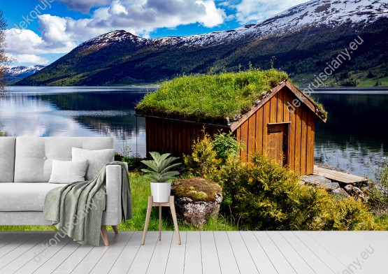Wizualizacja fototapety z widokiem na drewnianą chatkę przy jeziorze z trawiastym dywanem na dachu, na tle gór Norwegii. Fototapeta do pokoju dziennego, sypialni, salonu, biura, gabinetu, przedpokoju i jadalni.