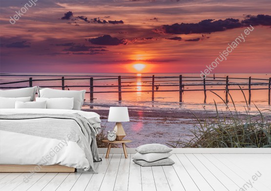 Wizualizacja fototapety widokiem na piaszczystą plażę i morze zabarwione kolorami zachodzącego słońca. Fototapeta do pokoju dziennego, sypialni, salonu, biura, gabinetu, przedpokoju i jadalni.