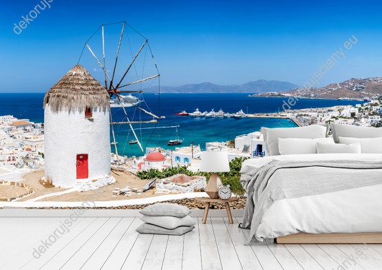 Wizualizacja fototapety z widokiem na tradycyjny wiatrak górujący nad białymi domami greckiego miasta, na wyspie Mykonos. Fototapeta do pokoju dziennego, sypialni, salonu, biura, gabinetu, przedpokoju i jadalni.