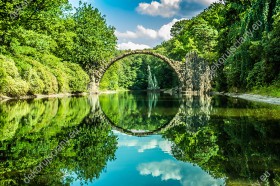 Wzornik fototapety przedstawia kamienny most w nad wodą, w wiosennych barwach soczystej zieleni. Miejsce  Kromlau w Niemczech. Fototapeta przeznaczona do sypialni, salonu, biura, gabinetu, pokoju młodzieżowego.