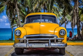 Wzornik obrazu z żółtym retro samochodem amerykańskim zaparkowanym pod palmami na Kubie. Obraz do pokoju dziennego, młodzieżowego, sypialni, salonu, biura, gabinetu, przedpokoju i jadalni.