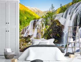 Wizualizacja fototapety z malowniczym widokiem na górskie wodospady otoczone wiosennymi drzewami. Fototapeta do pokoju dziennego, sypialni, salonu, biura, gabinetu, przedpokoju i jadalni.