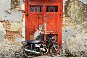 Wzornik obrazu przedstawia motocyklistę siedzącego na motorze, na tle starych, czerwonych drzwi. Obraz do pokoju dziennego, młodzieżowego, sypialni, salonu, biura, gabinetu, przedpokoju i jadalni.